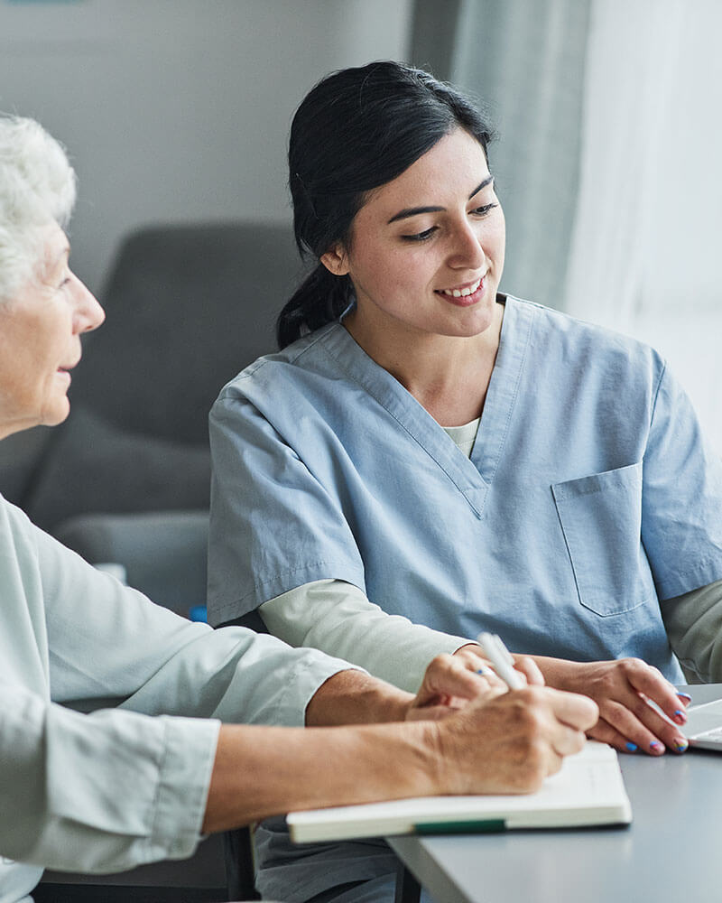 Young female nurse and elderly woman at a desk looking at computer